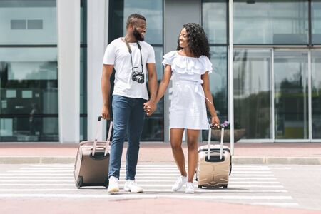 Happy african newlyweds enjoying honeymoon trip, arrived to airport with luggage