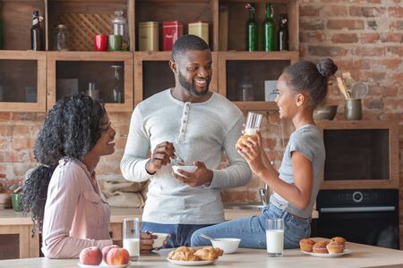 Friendly african american family of three talking at kitchen during breakfast, free space