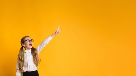 Look There. Happy Elementary Student Girl Pointing Finger Up Over Yellow Studio Background. Panorama With Copy Spaceの写真素材