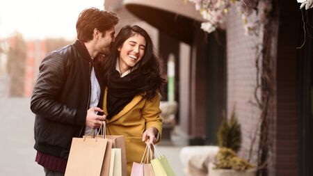 Shopping together. Man whispering in woman ear pleasant words, walking after shopping, free space