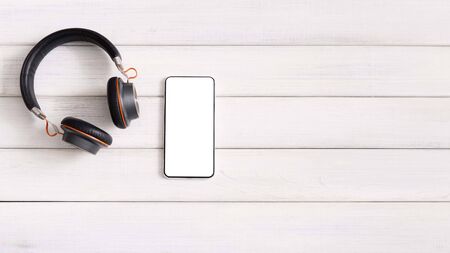 Best music app. Smartphone with blank screen and modern wireless headphones on wooden background, panoramaの写真素材