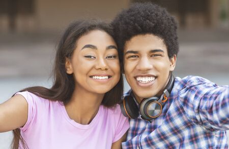 Two cheerful african american teenagers taking selfie outdoors, posing to cameraの写真素材
