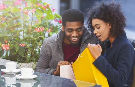 Black couple with shopping bags drink coffee at cafe, checking their purchases, empty space