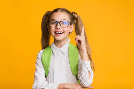 Idea Concept. Excited Primary School Girl Pointing Finger Up Over Yellow Studio Background. Empty Spaceの写真素材