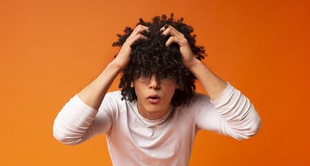 Troubles concept. Shocked emotional african man with bushy hairstyle rending his hair in desperate gesture, orange studio backgroundの写真素材