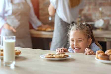Charming little girl looking with joy sweets, kitchen interior, copy spaceの写真素材