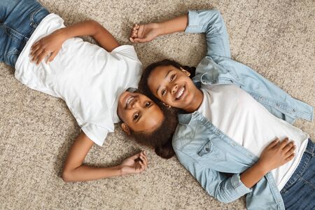 Two happy african sisters laying on carpet face to face at homeの写真素材