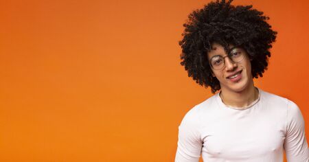 Portrait of black guy in glasses with bushy hairstyle, orange studio background, panorama with empty spaceの写真素材