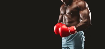 Boxing concept. Cropped image of strong african boxer wearing red boxing gloves over black studio background, free spaceの写真素材