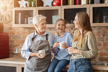 Female family drinking tea and laughing, mom, daughter and granny spending time together at kitchen, copy spaceの写真素材