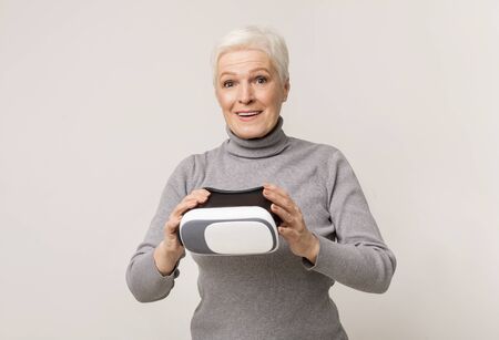 Modern technology and senior age. Elderly woman amazed of experiencing virtual reality after using VR headsetの写真素材