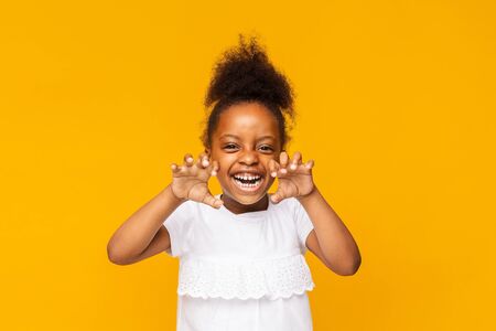 Funny tiger. Cute playful little african girl is showing claws, orange studio backgroundの写真素材