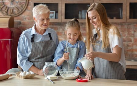 Young cute girl learning how to make pastry with mother and grandmother, kitchen interiorの写真素材