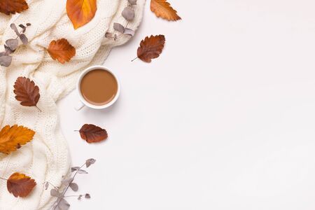 Golden autumn concept. Creative flat lay of fallen leaves, warm scarf and coffee on white background...