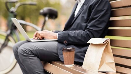 Businessman dont have time for snack, using laptop in park, sitting on benchの写真素材