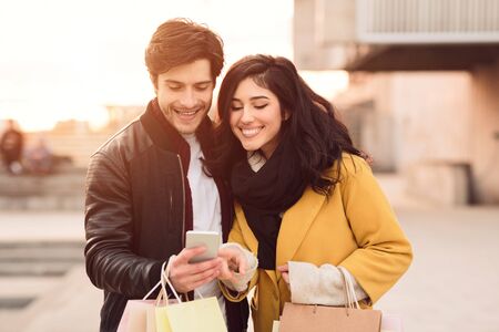 Happy couple with cellphone inviting friends for walk enjoying autumn evening