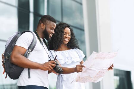 Happy african tourists searching map, planning route near airport, free space