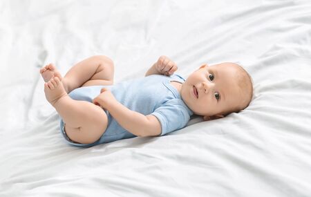 Portrait of cute newborn baby lying on bed in blue bodysuit, copy space
