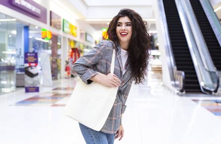 Happy woman with blank eco cotton bag shopping in city mall and waiting for friend