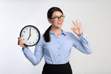 Meet Deadline. Positive Businesswoman Holding Clock Gesturing OK On White Studio Background.