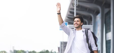 Catching a taxi. Young man waving hand near airport building, panorama with empty spaceの写真素材