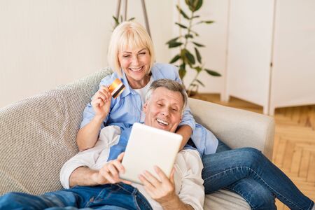 Modern elderly couple shopping online with tablet and credit card at home