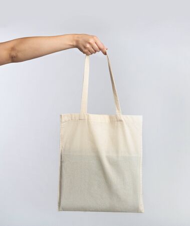 Female Hand Holding White Blank Eco Bag Over Gray Studio Background. Ecology And Minimalism Conceptの写真素材