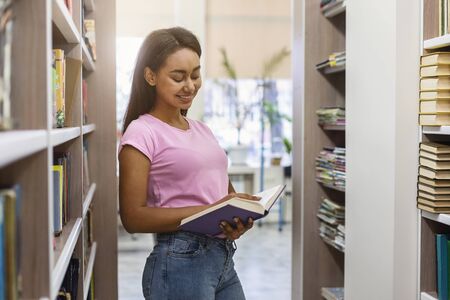 Cheerful african american girl reading book, spending time at bookstore, copy space