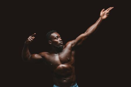 Artistic african bodybuilder posing over black studio background, imitating ancient warrior, copy spaceの写真素材