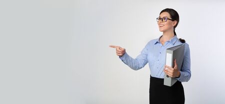 Look There. Smiling Businesswoman Pointing Finger Aside Holding Folder Over White Background In Studio. Panorama, Copy Spaceの写真素材