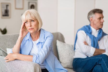 Sad senior woman after arguing with husband, sitting on sofa in living roomの写真素材