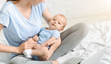 Multitasking. Young woman looking after her baby son while working on laptop at homeの写真素材