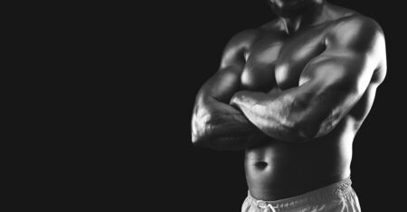 Muscular body of african male fitness model, arms crossed, black studio background, cropped, panorama with copy spaceの写真素材