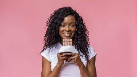African Woman Want To Eat Milk Chocolate, smiling at camera over pink background, copy spaceの写真素材