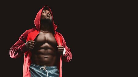 Black muscular fighter in red hoodie, black studio background, panorama with copy spaceの写真素材