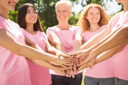 Smiling Diverse Women Wearing Breast Cancer Pink Ribbon T-Shirts Holding Hands Outdoor In Park....