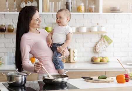 Domestic life. Mother cooking lunch with baby at kitchen, free spaceの写真素材
