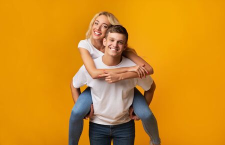 Piggyback ride. Young man carrying girlfriend on his back, yellow background with copy space.