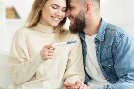 Happy couple checking pregnancy test with positive result, man embracing womanの写真素材