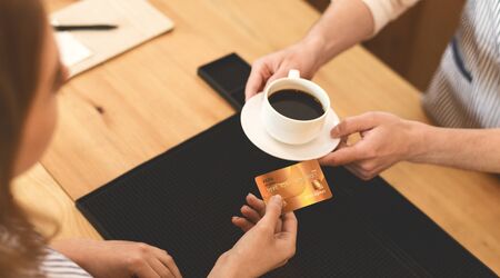 Easy pay system. Unrecognizable Woman giving gold credit card for tasty morning coffee in cafe, panoramaの写真素材