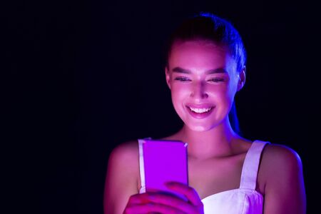 Happy woman using phone, illuminated by neon lights in studio, copy space