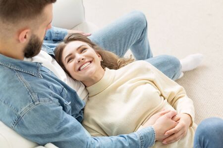 Loving couple relaxing on sofa, cozy warm leisure day, woman lying on man legsの写真素材