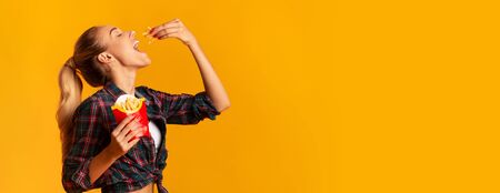 Cheerful Girl Eating French-Fried Potatoes Over Yellow Studio Background. Cheat Meal And Fast Food....