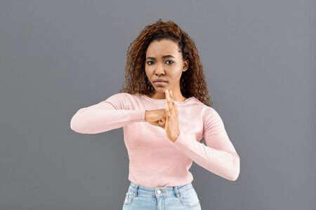 Beautiful serious mixed race woman showing lock sign, resting her fist in palm on grey background