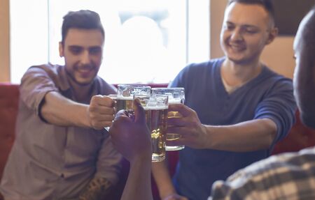 Happy multiracial young mates clinking glasses with beer together, spending time at pub, free spaceの写真素材