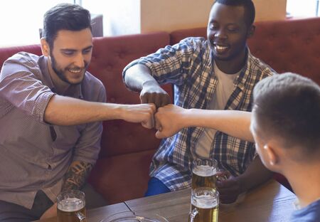 Brotherhood concept. Three mixed race mates bumping fists together, drinking beer at bar