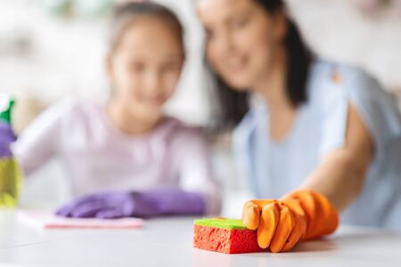 Little girl helping mother to clean flat. Closeup, selective focus on sponge