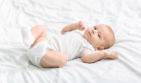 Portrait of cute little baby in bodysuit lying on bed and looking to camera, panorama with copy...