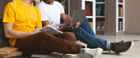 Technologies and education. Two male multi ethnic students studying at library, sitting on floor,...