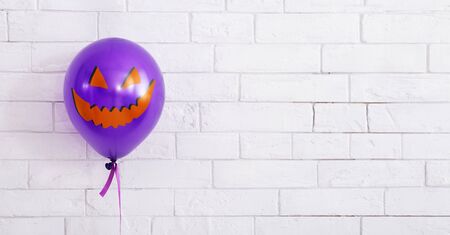 Halloween concept. Celebrating purple balloon with evil smile on white bricks wall background, panorama, copy spaceの写真素材